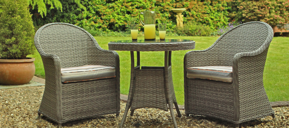two grey cane furniture chairs and a glass table situated in a garden